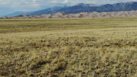 aerial cinematic drone late summer opening view entrance of the great sand dunes national park colorado rocky mountain 14er peaks crisp golden yellow tall grass blue sky backward movement pan up