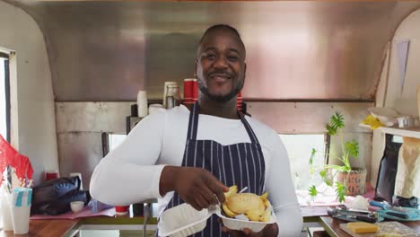 sonriente propietario de un negocio afroamericano que tiene una comida para llevar en un camión de comida