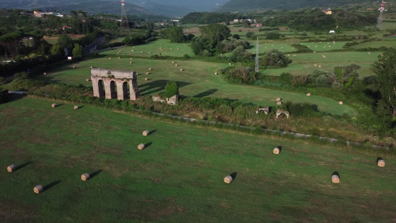 antiguo acueducto romano en lazio, italia, rodeado de campos verdes y balas de heno en la luz dorada, vista aérea