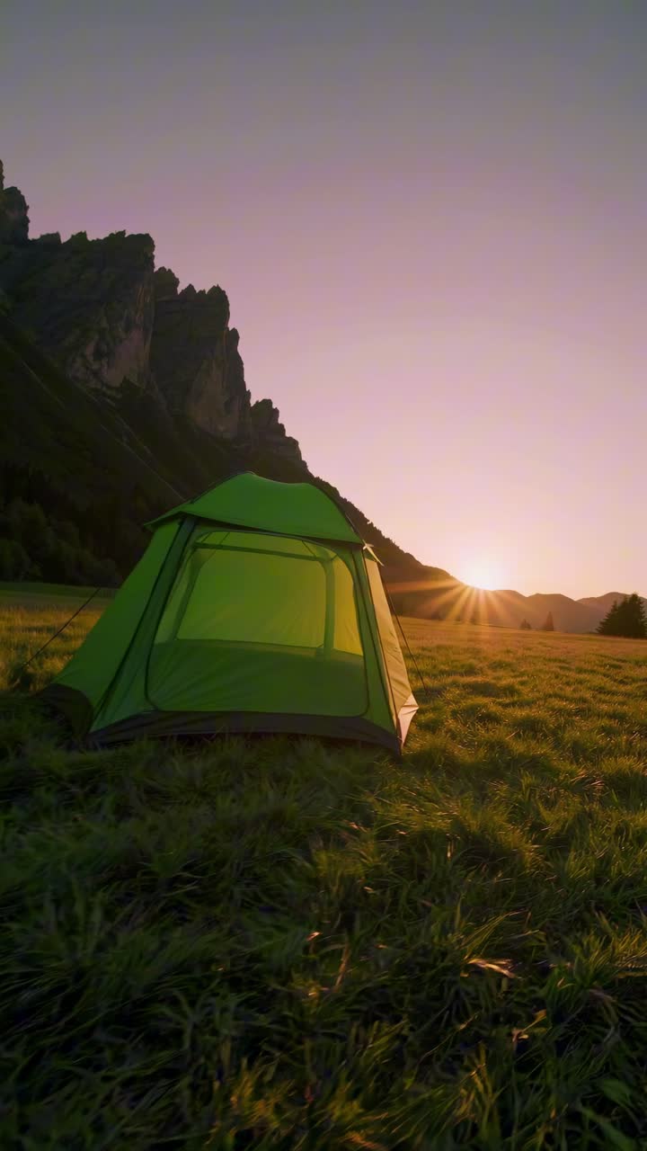 En rolig landskabsvideo fanger et grønt telt på en græsmark ved solnedgang med tårnhøje bjerge