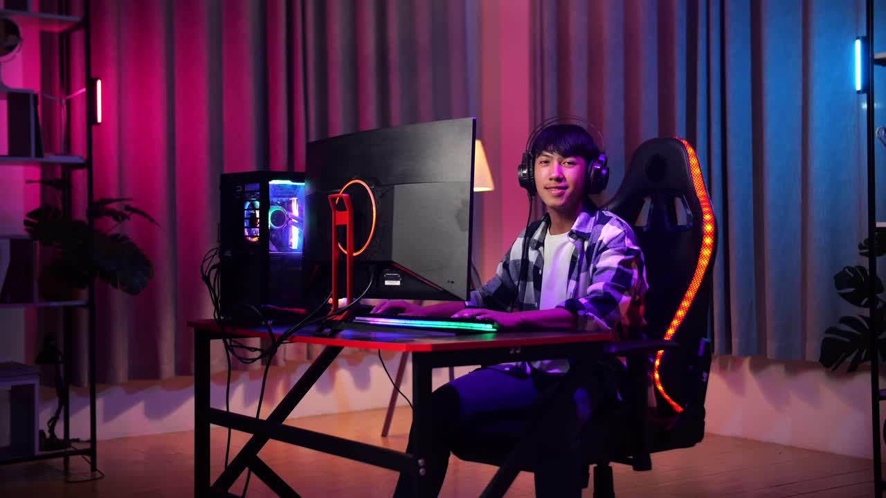 Ragazzo adolescente asiatico gamer che sorride alla telecamera mentre gioca a un videogioco al computer.