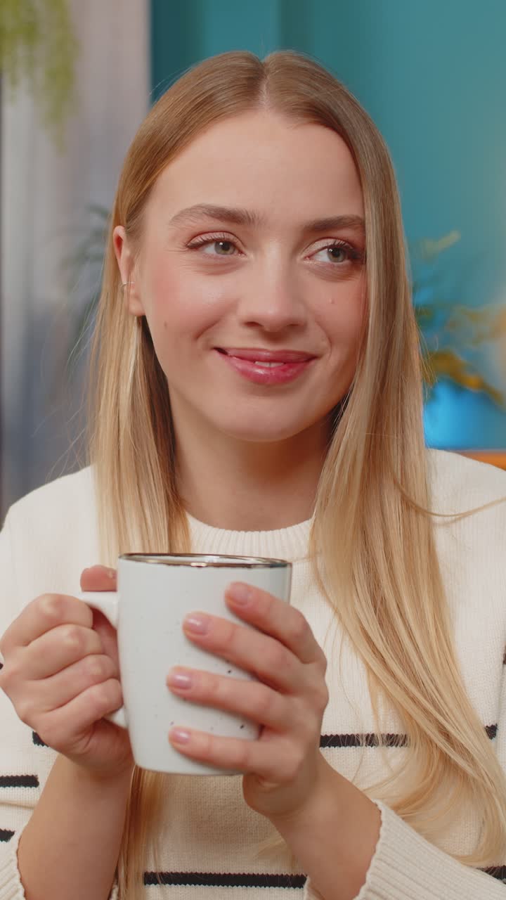 Caucasian woman enjoying hot tea on sofa holding cup both hands relaxing indoors calm comfortable