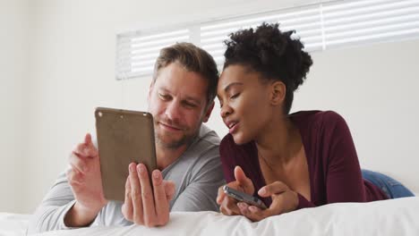 Video-De-Una-Feliz-Pareja-Diversa-Usando-Una-Tableta-En-La-Cama-Y-Hablando