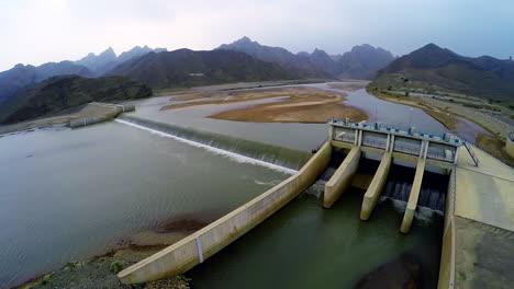 Aerial-view-of-spillway-of-a-dam,-Beautiful-majestic-mountains-in-the-back-of-the-dam