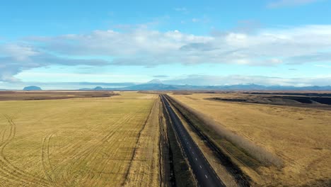 Coche-De-Retroceso-Aéreo-Que-Conduce-Un-Camino-Panorámico-Interminable-En-El-Paisaje-Rural-De-Islandia
