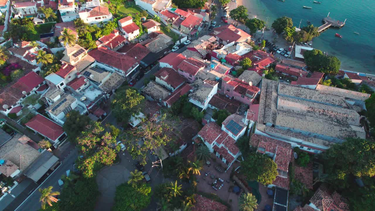 Drone flying over waterfront Houses with roof tiles toward to turquoise water bay in B&uacute;zios