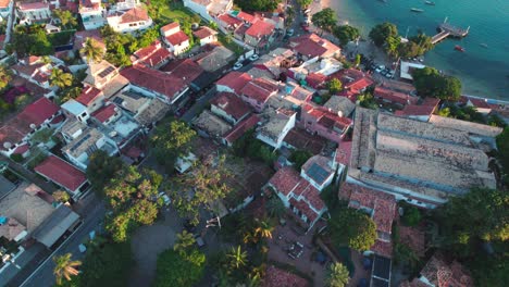 Drone-Volando-Sobre-Casas-Frente-Al-Mar-Con-Tejas-Hacia-La-Bahía-De-Agua-Turquesa-En-Búzios