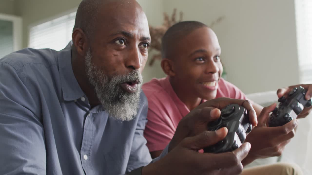 video de un padre y un hijo afroamericanos felices jugando videojuegos