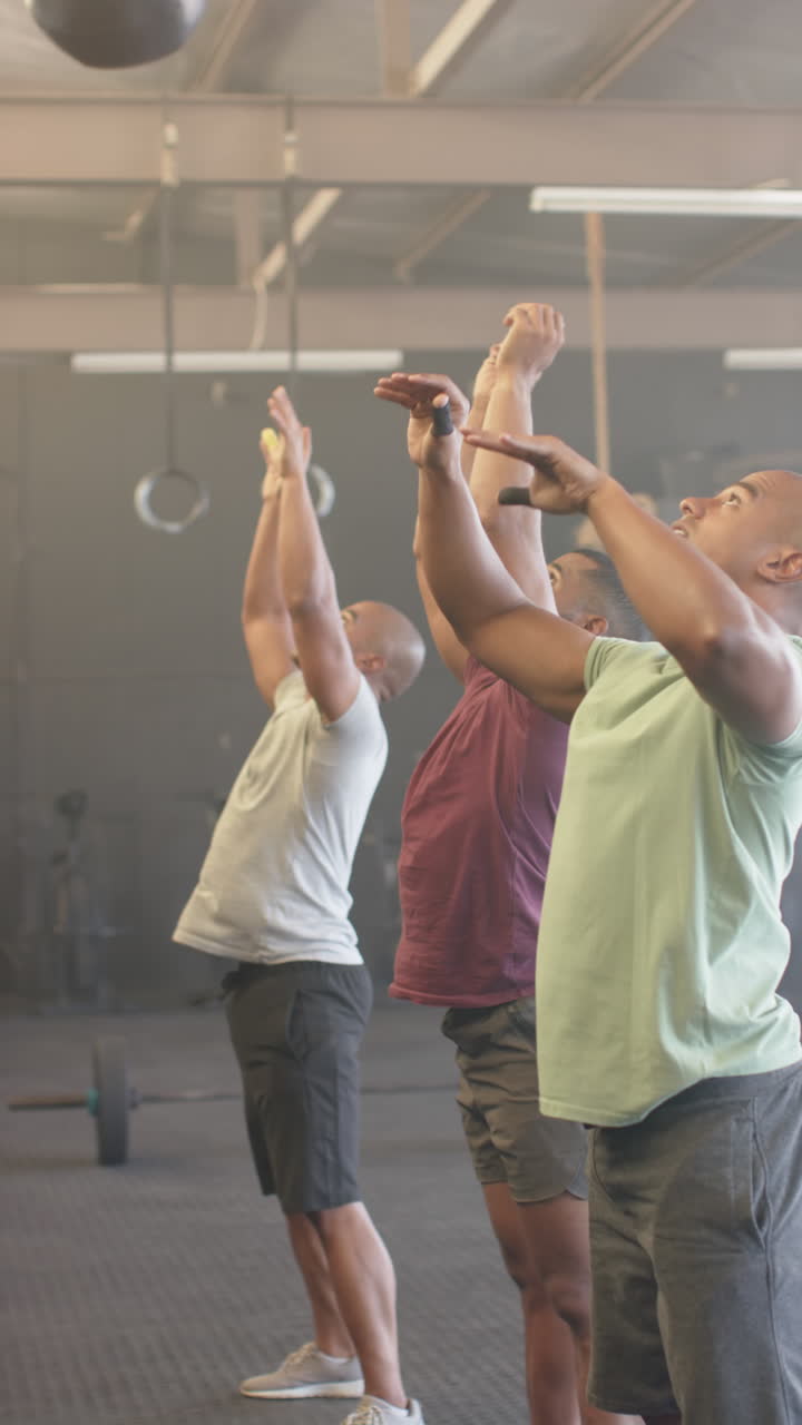 Vertical video of diverse sports people lifting medicine balls at gym in slow motion