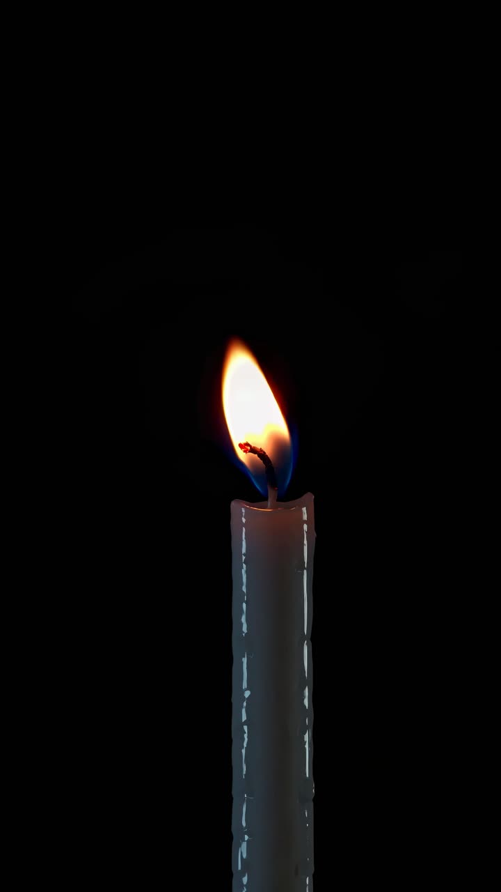Close-up video of a lit candle against a black background, capturing the flickering flame