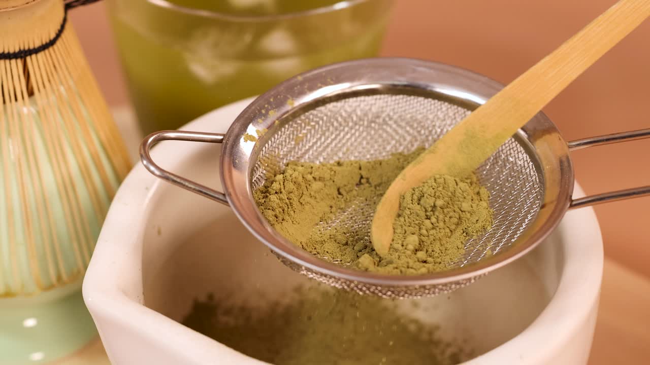 Matcha powder sifted through fine mesh strainer into bowl, warm lighting, close-up, steady camera