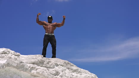 African american sportsman posing on blue sky background. Dark skinned athlete showing his strong arm muscles outdoors. View from below.