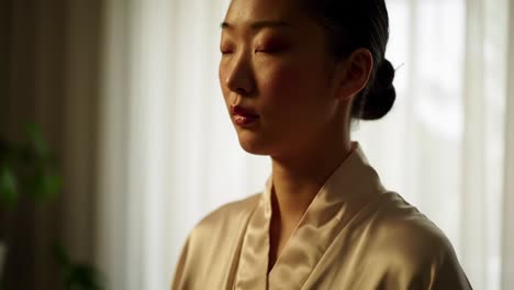 a serene moment of reflection: a calm woman in a silken white robe with closed eyes, bathed in soft natural light amidst a cozy indoor setting