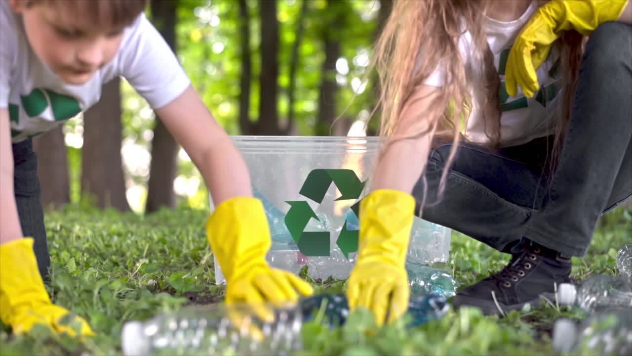Niño y niña recogiendo basura de plástico en un contenedor en un parque contaminado, con símbolos de reciclaje en las camisetas. Cámara lenta