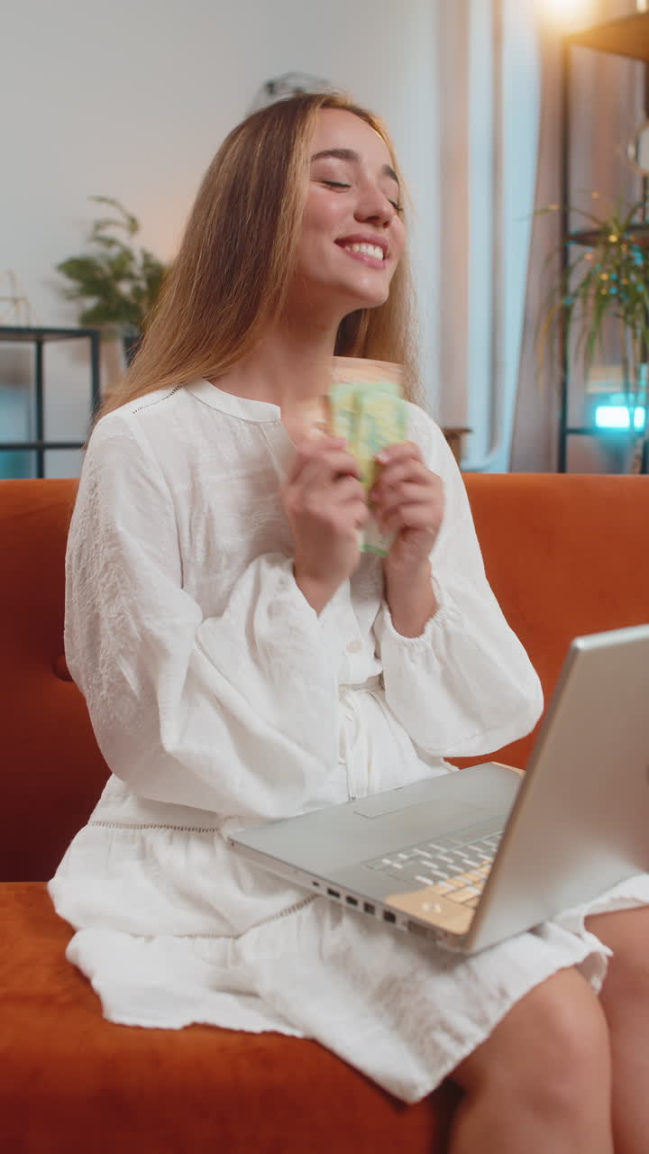 Rich happy young woman counting money euro cash using smartphone calculator sitting at home