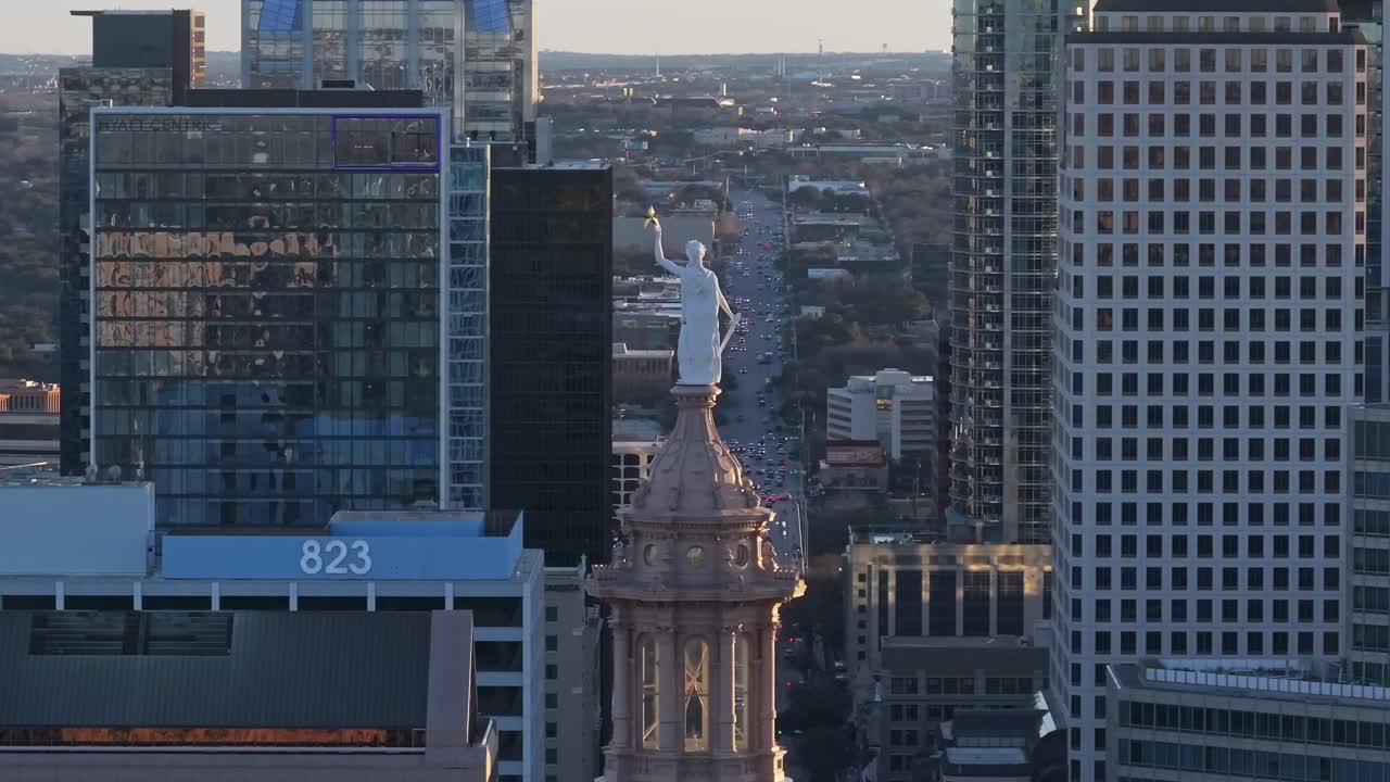 A slow zoomed-in drone shot with parallax circling the Texas State Capitol building in Austin with Congress Ave. in the background with the sunset backlighting the Goddess of Liberty statue on top