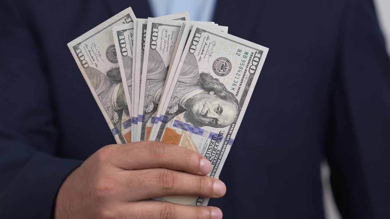 Uomo d'affari in abbigliamento professionale che mostra una pila di banconote da un dollaro in primo piano, concetto di conteggio del denaro, video 4K