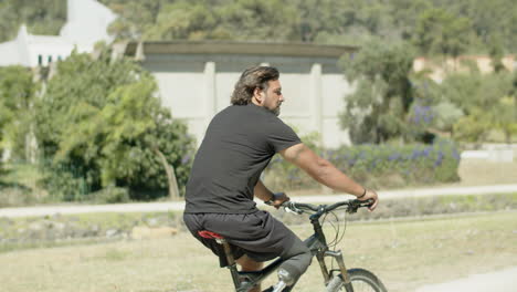 Tracking-shot-of-serious-man-with-disability-riding-bike-in-park