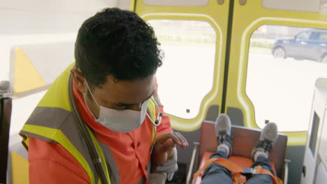 paramedic wearing facial mask touching the hand and arm of a patient lying on the stretcher inside an ambulance