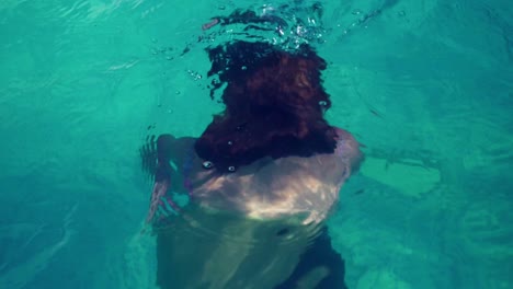 Hand-held,-slow-motion-shot-of-a-young-redhead-woman-swimming-in-a-pool