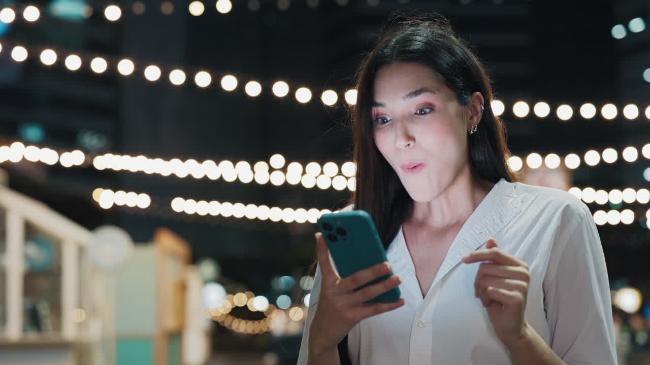 Woman Looking at Smartphone with Excited Expression at Night Market