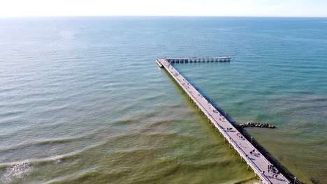 people walking on palanga bridge on sunny day with calm sea, aerial ascend view