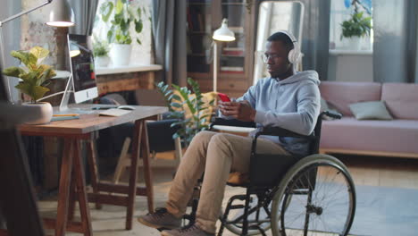 man in wheelchair using smartphone in home office