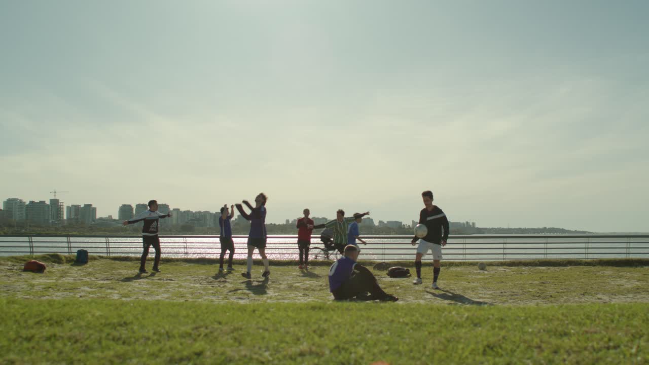 Friends playing football soccer by the waterfront on a sunny day with a city skyline in the background