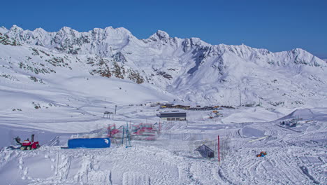 time lapse shot of snow park being constructed by snow groomers in white winter landscape - snowy mountain range backdrop