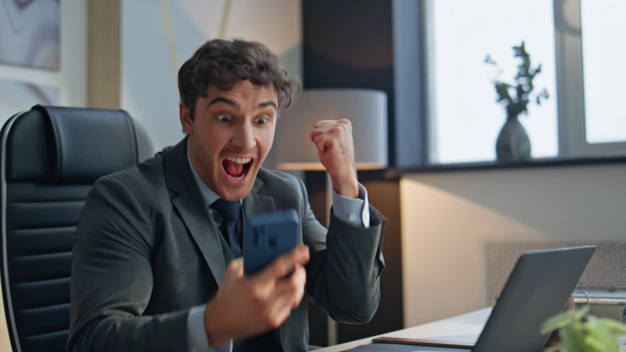 Chefe surpreso olhando para o smartphone no escritório, close-up. Homem animado comemorando o sucesso.