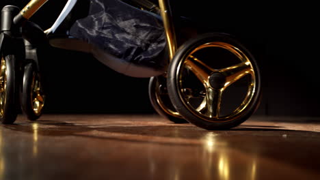 lower part of dark blue baby stroller with golden elements. modern perambulator on the smooth floor in the dark room.