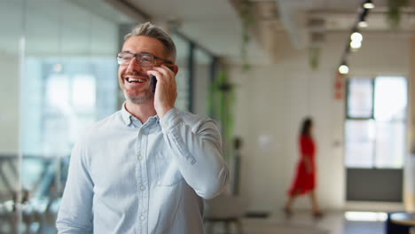 mature businessman standing in modern open plan office talking on mobile phone