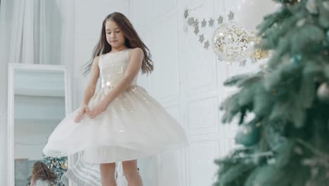 beautiful girl spinning near christmas tree in white dress.