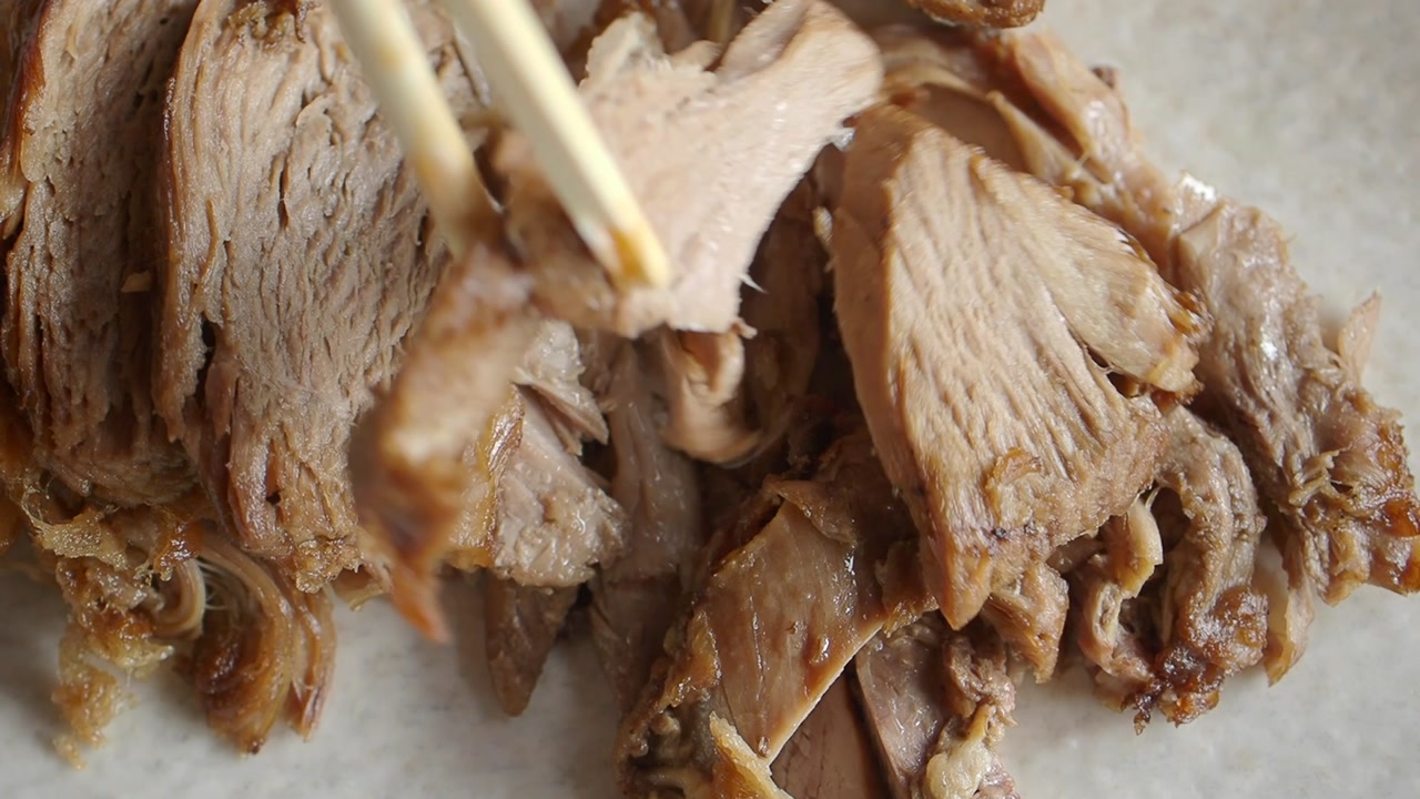 Close-up of chopsticks picking up a piece of sliced braised pork