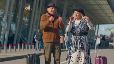 elderly husband wife retirees tourists go to airport terminal for boarding with luggage on wheels