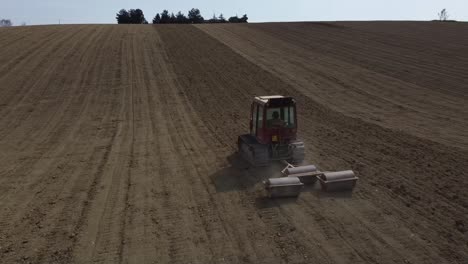 drone follow a red small tractor in rolling soil operation for seedbed preparation in uphill countryside agricultural farm