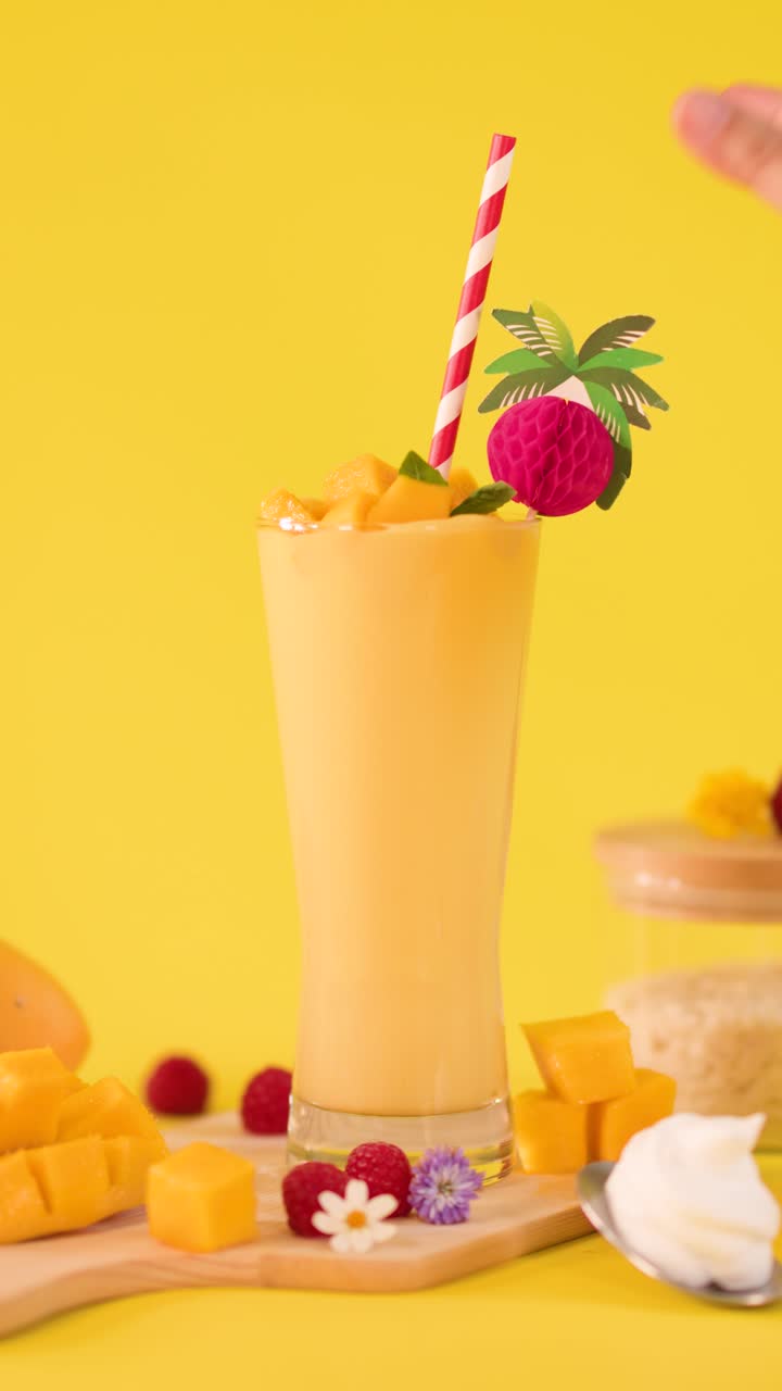 Primo piano giallo brillante di frullato di mango mentre una mano aggiunge uno spiedino decorativo giocoso di frutta tropicale