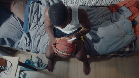 black sportsman sitting at home and writing autograph on the ball