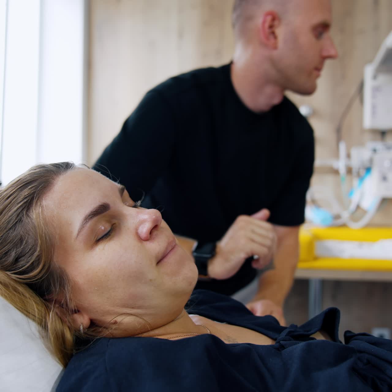 Woman suffering contractions lies in bed. Husband stands leaned to her talking. Close up