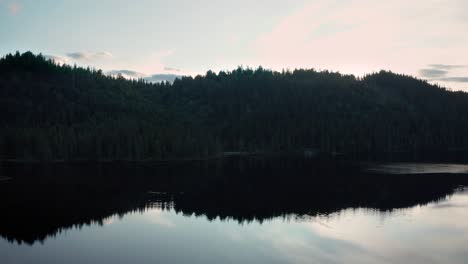 mirrored reflection of forested mountain in lake surface, twilight aerial