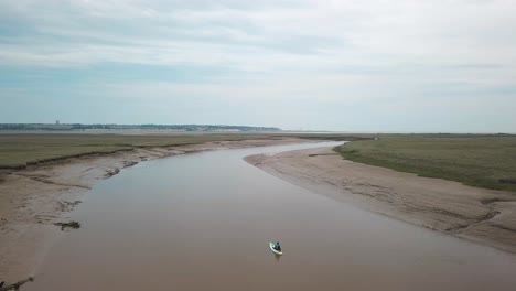 Man-kayaking-on-meandering-river,-drone-pans-to-the-right-with-beautiful-landscape-in-the-background