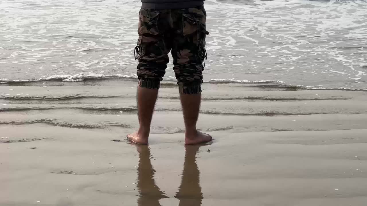 Close up shot of small waves touching persons feet in army half pant in a beach during daytime in Bengal, India