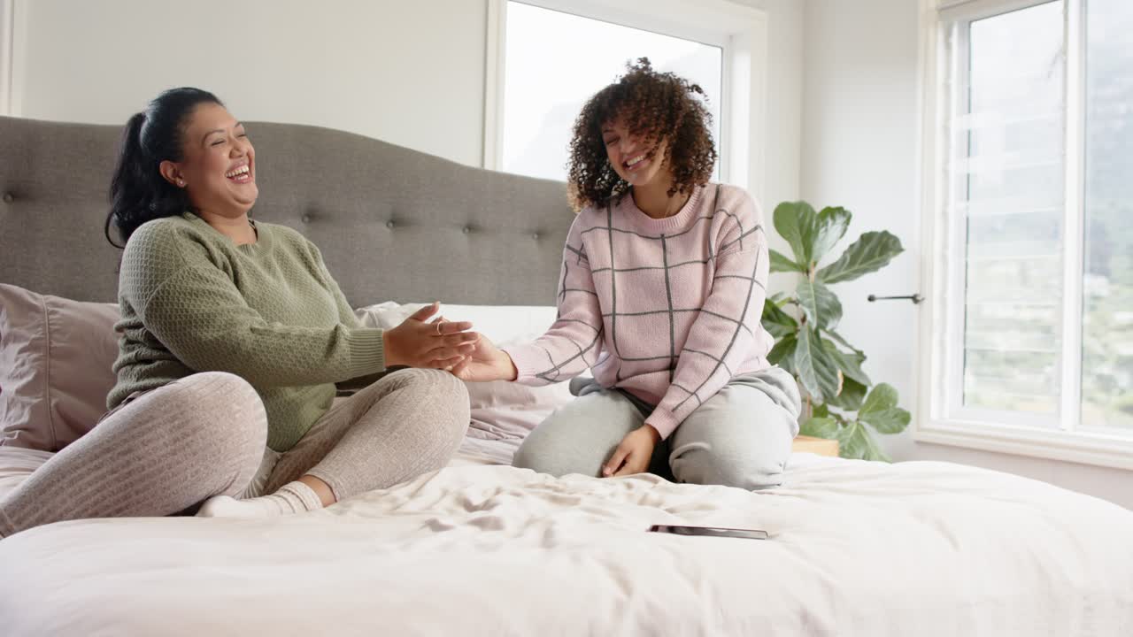 Veninder, der sidder på sengen og klemmer og kilder hinandens hænder, mens de griner sammen for sjovt samvær