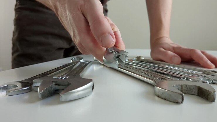 Man choosing small adjustable wrench, multiple spanners on worktop