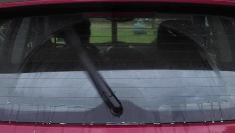 dirty back window of a small hatchback car being washed by a rear wiper