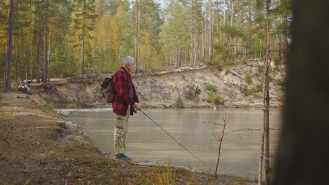 man-is-angling-alone-in-forest-river-using-rod-standing-on-coast-at-fall-day-enjoying-calmness-and-nature