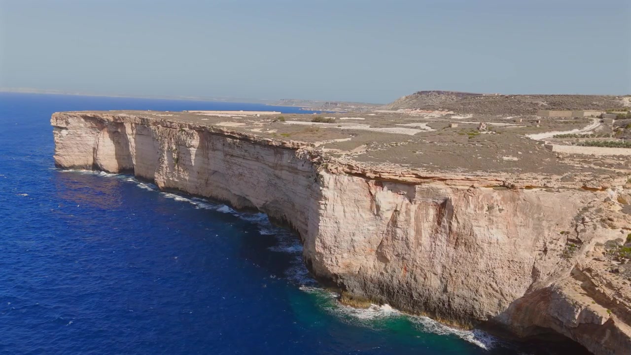 Vola sopra le splendide scogliere di Malta e ammira l'incantevole gioco di luci e ombre sulle coste rocciose, rivelando la bellezza costiera mozzafiato dell'isola