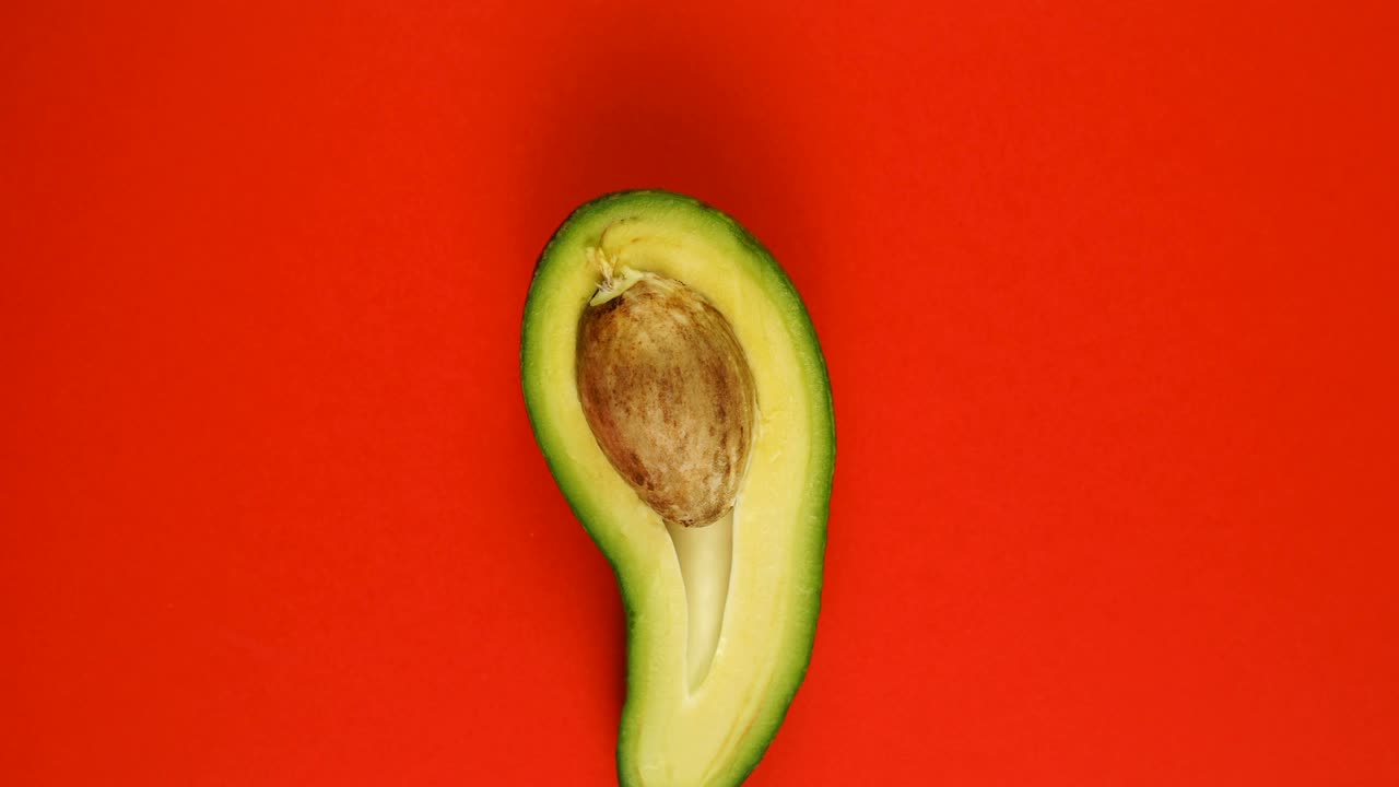 Vista dall'alto di avocado verde rotante, tagliato a metà con nocciolo su sfondo rosso