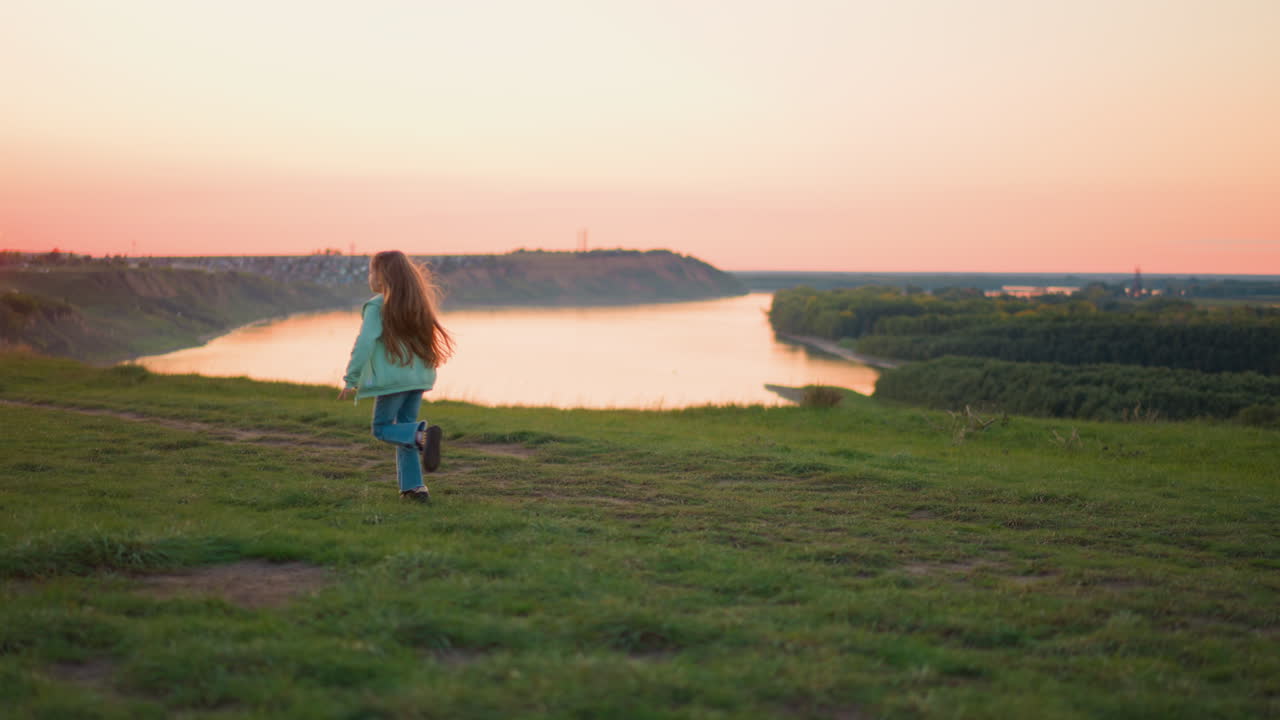 아이는 해가 지는 초원을 따라 달린다 장난스러운 긴 머리카락의 소녀는 저녁 강변에서 산책하는 것을 즐긴다.