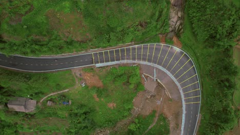 Tranquila-Chicana-De-Montaña:-Vista-Aérea-Con-Dron-De-Ciclistas-En-Una-Carretera-Panorámica,-Casa-De-Madera,-Formación-Rocosa-Y-Exuberante-Vegetación-Verde-Por-Todas-Partes